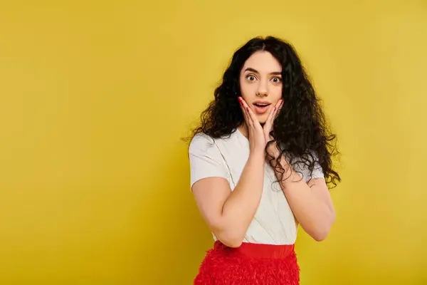 Young brunette woman with curly hair, wearing a red skirt, expresses emotions by covering her face with her hands. — Stock Photo