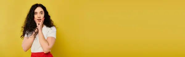 Une jeune femme brune élégante aux cheveux bouclés pose émotionnellement devant un mur jaune vibrant. — Photo de stock