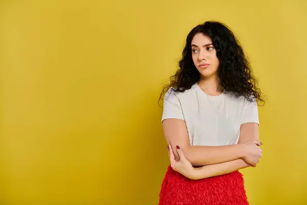 A stylish young woman with curly hair stands confidently with crossed arms against a vibrant yellow backdrop. — Stock Photo