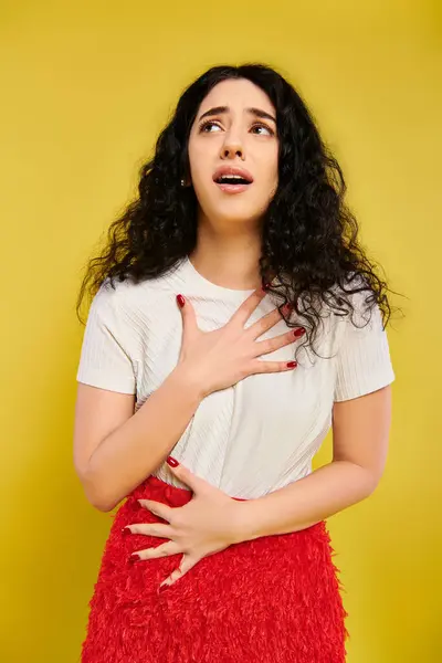 Giovane, donna bruna con i capelli ricci, posa elegantemente con le mani sul petto, mostrando emozioni serene in abbigliamento elegante. — Foto stock