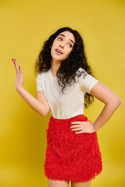 A young brunette woman with curly hair poses in a striking red skirt, showcasing her emotions in a studio with a yellow background. — Stock Photo
