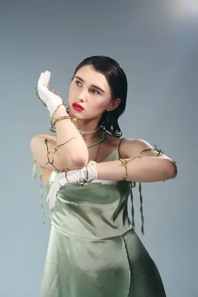 A young beautiful woman with red lips poses in a green dress, white gloves in a studio setting on a grey background. — Stock Photo