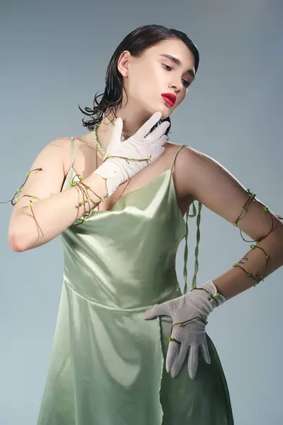 Eine junge schöne Frau mit roten Lippen posiert in einem grünen Kleid und weißen Handschuhen in einem Studio vor grauem Hintergrund. — Stockfoto