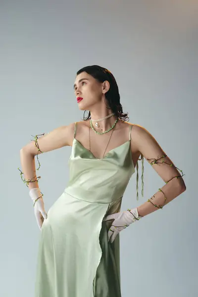 A young beautiful woman with red lips elegantly poses in a green dress and white gloves in a studio setting on a grey background. — Stock Photo