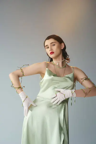 A young and beautiful woman with red lips poses gracefully in a green dress and white gloves in a studio setting on a grey backdrop. — Stock Photo