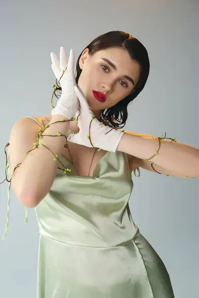 Uma mulher jovem e bonita com lábios vermelhos faz uma pose em um vestido verde e luvas brancas em um estúdio em um cenário cinza.. — Fotografia de Stock