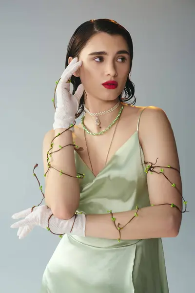 A young, beautiful woman with red lips poses gracefully in a green dress and white gloves in a studio setting on a grey background. — Stock Photo