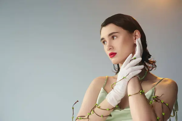 A young beautiful woman with red lips poses in a green dress and white gloves in a studio setting on a grey background. — Stock Photo