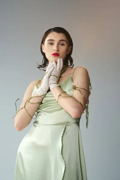 A young beautiful woman with red lips posing in a green dress and white gloves in a mystical studio setting on grey. — Stock Photo