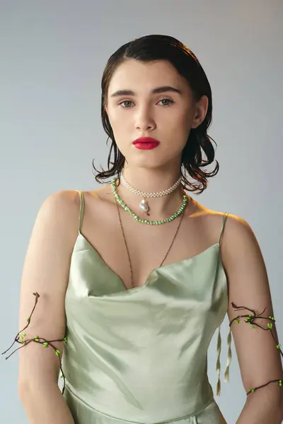 Eine schöne junge Frau mit roten Lippen posiert anmutig in einem grünen Kleid und einer Halskette in einem Studio vor grauem Hintergrund. — Stockfoto