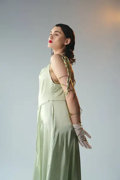 A young woman with red lips striking a pose in a green dress and gloves in a studio setting on a grey background. — Stock Photo