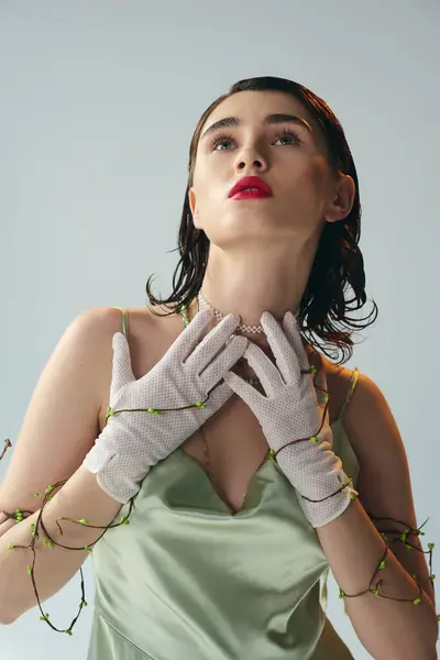 Une jeune et belle femme aux lèvres rouges pose en robe verte et gants blancs dans un décor studio sur fond gris. — Photo de stock