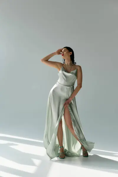 A young, beautiful woman poses in a flowing dress and elegant gloves in a studio against a grey backdrop. — Stock Photo