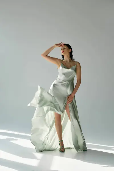 A beautiful young woman with red lips strikes a pose in a white dress and gloves in a studio, set against a grey backdrop. — Stock Photo