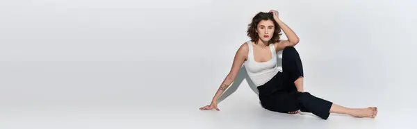 Une jeune femme en pantalon noir et débardeur blanc exécute gracieusement une pose de yoga dans un studio — Photo de stock