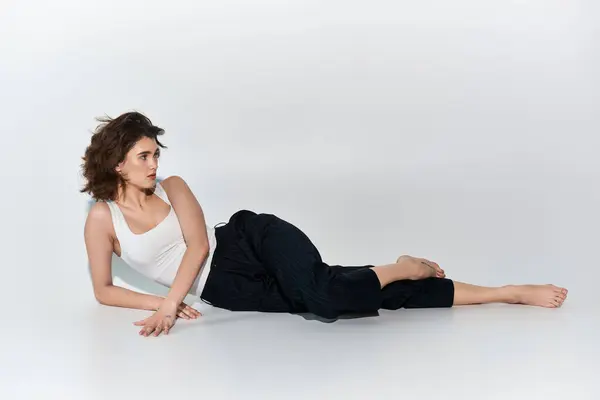 A young woman, dressed in black pants and white tank top, lies on the ground with her legs crossed in a serene and graceful pose. — Stock Photo