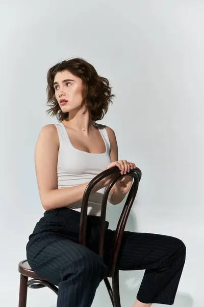 Uma jovem bonita posa graciosamente em uma cadeira de madeira, exalando elegância e confiança em um ambiente de estúdio. — Fotografia de Stock