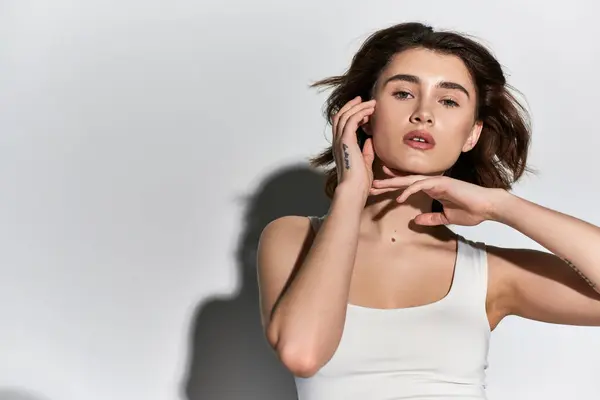 A stylish young woman in a white tank top in a sleek studio setting. — Stock Photo