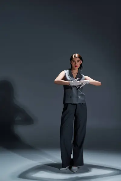 Una giovane donna elegante in un abito elegante si trova con fiducia al centro di un cerchio su uno sfondo grigio studio. — Foto stock
