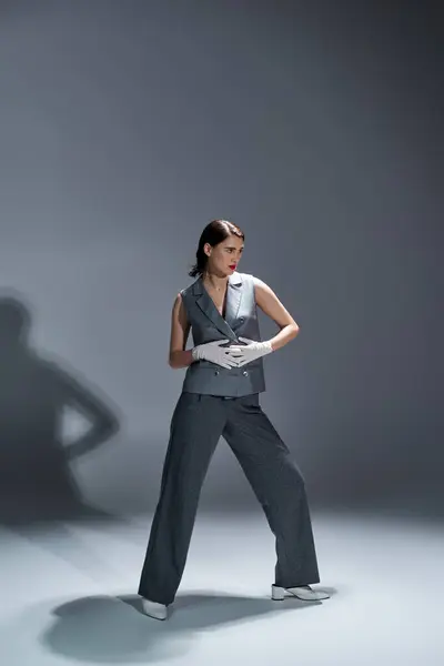 A stylish young woman posing in an elegant suit with a vest in a studio setting on a grey background. — Stock Photo