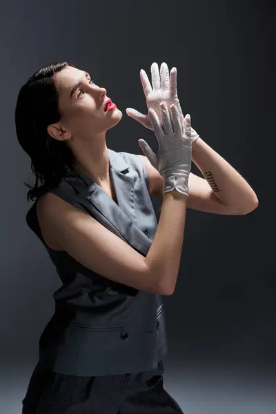 A stylish young woman in an elegant suit with a vest raising her hands in the air in a studio setting against a grey background. — Stock Photo