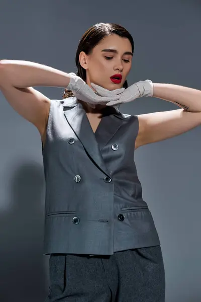 A stylish young woman in an elegant suit poses in gloves in a studio setting on a grey background. — Stock Photo