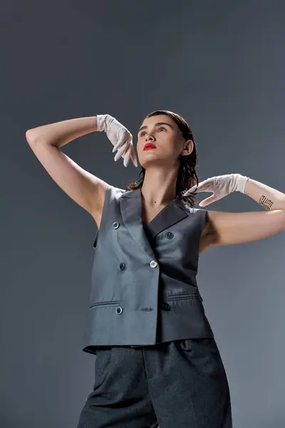 Stilvolle junge Frau posiert im eleganten schwarzen Anzug mit Weste und weißen Handschuhen in einem Studio vor grauem Hintergrund. — Stockfoto