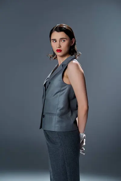 A stylish young woman strikes a pose in an elegant gray suit with a vest, accentuated by bold red lipstick, against a grey background. — Stock Photo