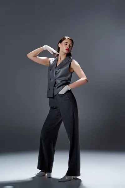 Stilvolle junge Frau in eleganter grauer Weste und Hose posiert selbstbewusst in einem Studio vor grauem Hintergrund. — Stockfoto