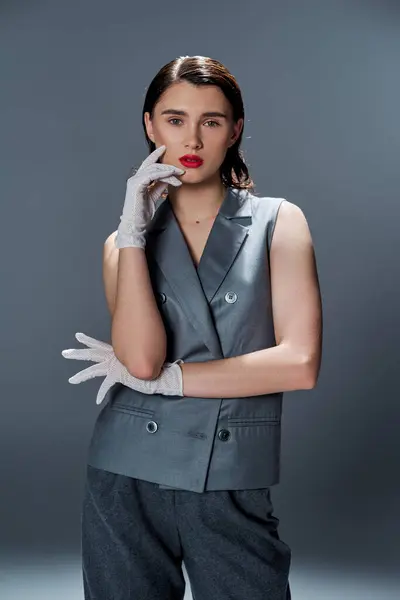 A stylish young woman poses in an elegant gray suit and white gloves against a studio backdrop. — Stock Photo