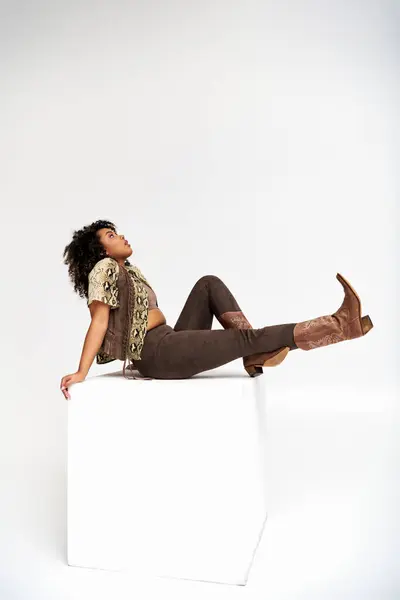Sophisticated trendy african american woman with animalistic print on attire sitting on white cube — Stock Photo
