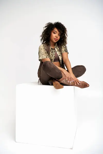 Beautiful african american woman in elegant attire sitting on white cube and looking at camera — Stock Photo