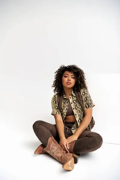 Appealing african american woman with print on her outfit sitting on floor and looking at camera — Stock Photo