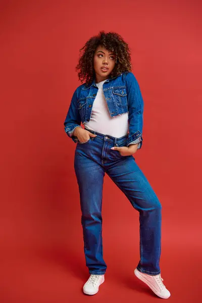 Well dressed young african american woman in stylish denim outfit looking away on red backdrop — Stock Photo