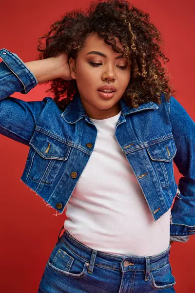 Sophisticated young african american woman in stylish denim outfit looking away on red backdrop — Stock Photo