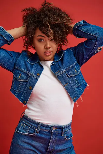 Well dressed african american woman in denim attire posing on red backdrop and looking at camera — Stock Photo