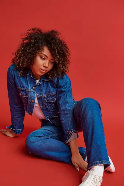 Elegant young african american woman in stylish denim outfit looking away on red vibrant backdrop — Stock Photo