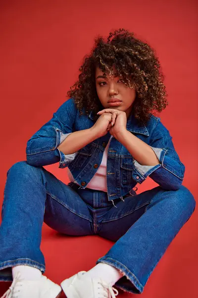 Fantasia afro-americana modelo feminino em traje de ganga olhando para a câmera e posando no fundo vermelho — Fotografia de Stock