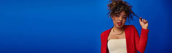 Elegante mujer afroamericana con el pelo recogido en traje vibrante mirando a la cámara, pancarta - foto de stock
