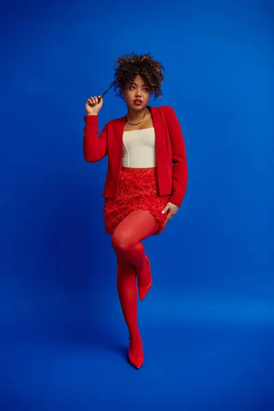 Verführerisch stilvolle afrikanisch-amerikanische Fashionista in lebendig elegantem Outfit, das vor blauem Hintergrund wegschaut — Stockfoto