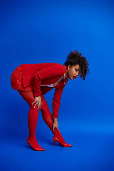 Chique sedutor afro-americano fashionista em roupa elegante vívida olhando para longe no pano de fundo azul — Fotografia de Stock