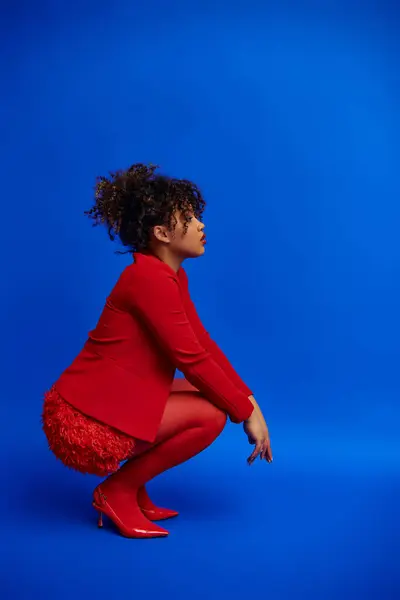 Graceful trendy african american fashionista in elegant outfit looking away on blue backdrop — Stock Photo