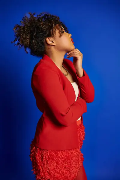 Raffinierte afrikanisch-amerikanische Frau in lebendiger Kleidung mit gesammelten Haaren, die vor blauem Hintergrund wegschaut — Stockfoto