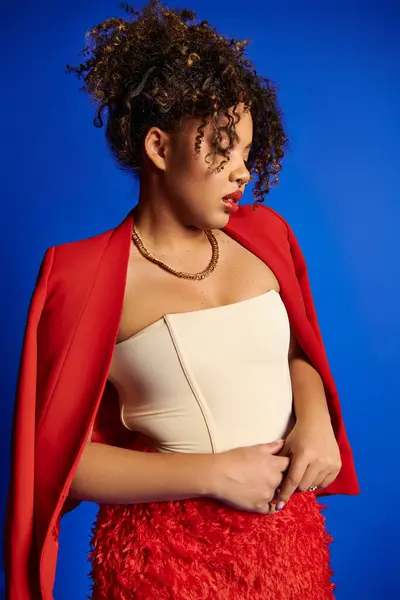 Refined stylish african american female model in vibrant outfit looking away on blue backdrop — Stock Photo