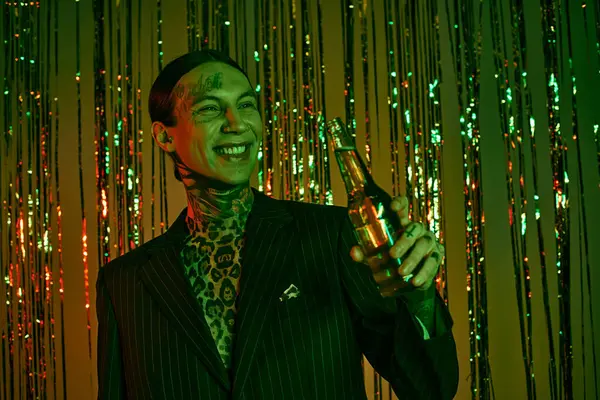 En una fiesta de rave, un hombre con traje y corbata sostiene una botella - foto de stock