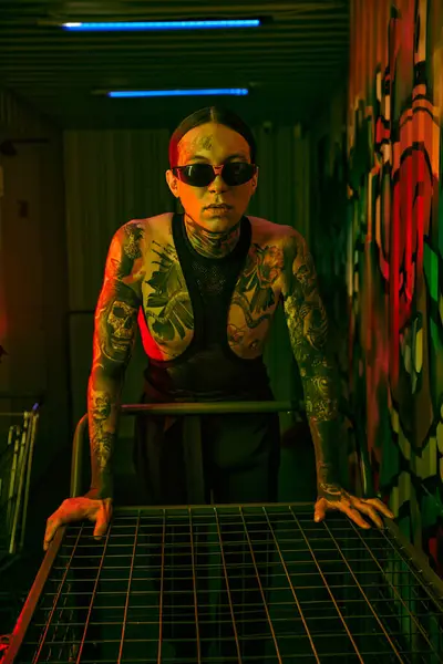Hombre con tatuajes y piercings delante de una mesa - foto de stock