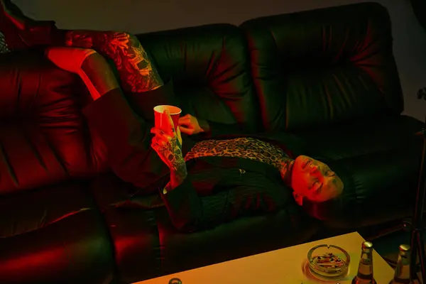 Eine Person, die bequem auf einer Couch liegt und ein Getränk in der Hand hält — Stockfoto