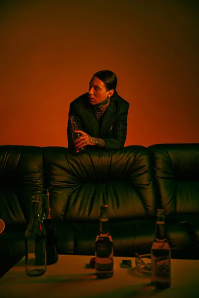 Чоловік сидить на дивані біля пляшок алкоголю — стокове фото