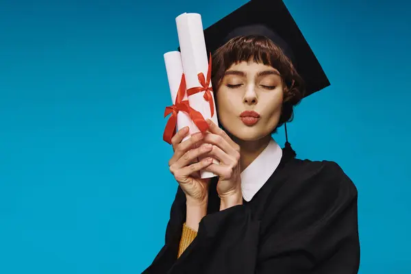 Felice laureata ragazza del college in abito e cappello accademico in possesso di diplomi con orgoglio, sfondo blu — Foto stock