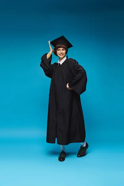 Excited graduated college girl in gown and cap smiling on blue background, accomplishment — Stock Photo